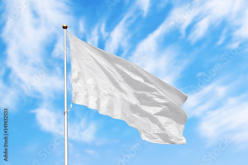 Blank white flag on pole waving in the wind in the background of cloudy sky. Colorful outdoor picture with empty flag mockup
