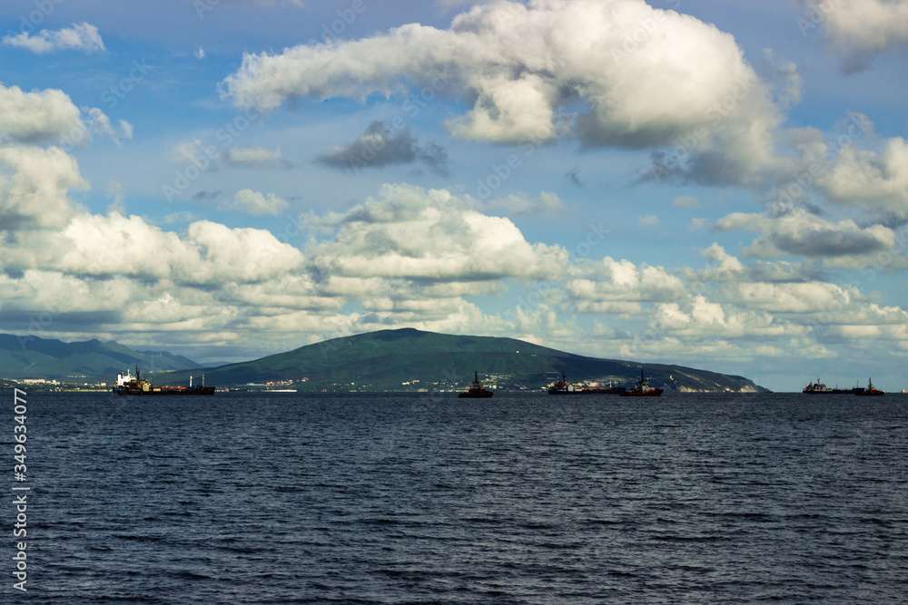 View at clouds on mountain and sea ship on the raid near the port in bay near Novorossiysk at sunny day.