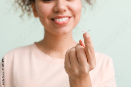 Young African-American woman with contact lens on color background