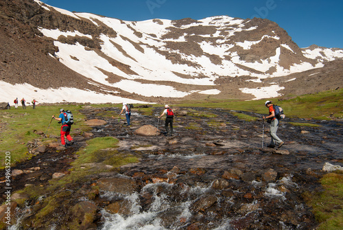 Montañeros vadeando el cauce de la laguna Hondera en la Cañada de Siete Lagunas, en el Parque Nacional de Sierra Nevada en el ascenso al pico Mulhacén (3479 m). photo