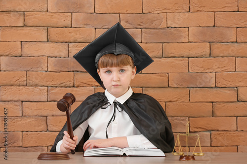 Portrait of little judge sitting at table against brick background photo