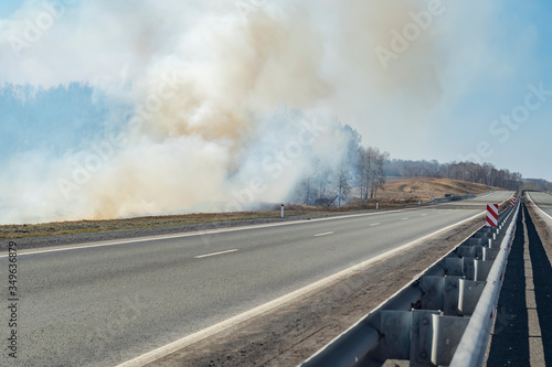 a strong fire, flame and a lot of smoke near the paved highway route, burning dry grass © Евгений Медведев