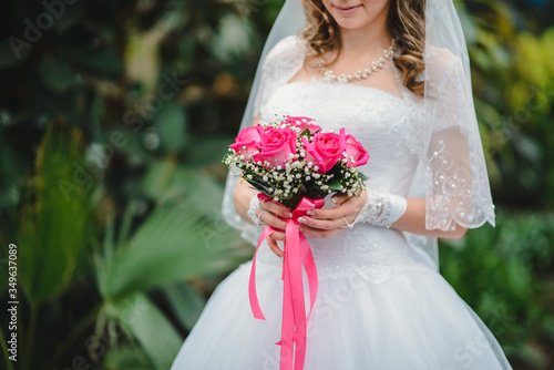 bride holding a bright bouquet of roses on the green background. Image with selective focus. 