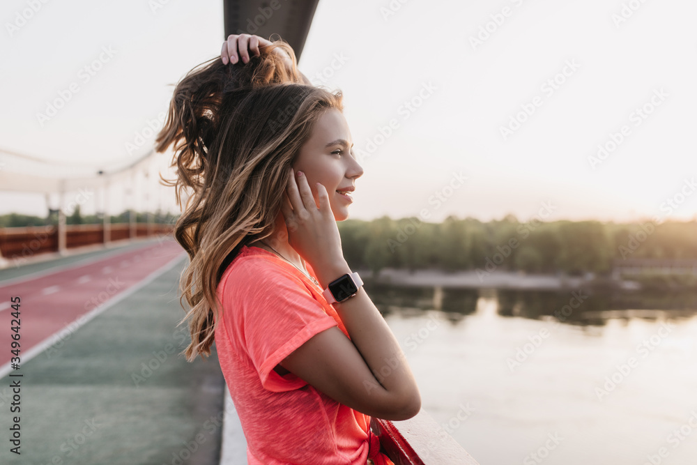 Ecstatic girl with smartwatch playing with her hair. Outdoor photo of amazing caucasian lady chilling after training.