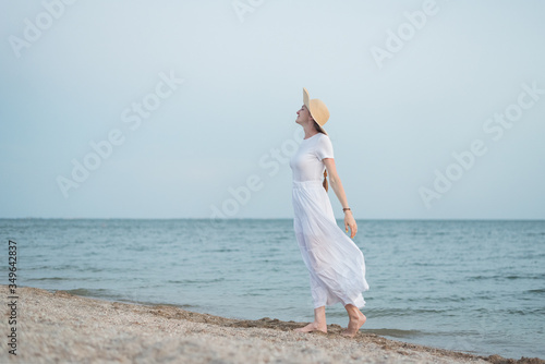 Beautiful young woman in white dress and hat on beach. Aristocrat girl on seaside