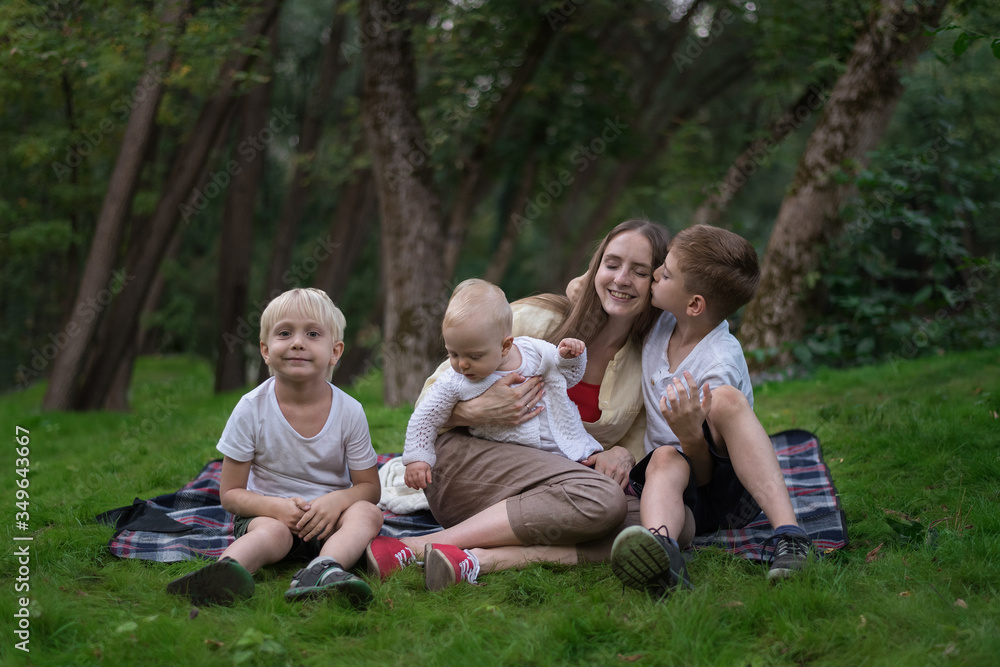 Happy family of four having picnic at meadow. Mother and three children sitting on picnic blanket Happy family of four having picnic at meadow. Mother and three children sitting on picnic blanket