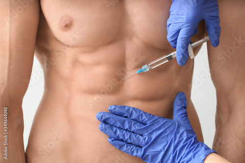 Obraz na plátně Muscular man receiving injection of steroids on light background, closeup