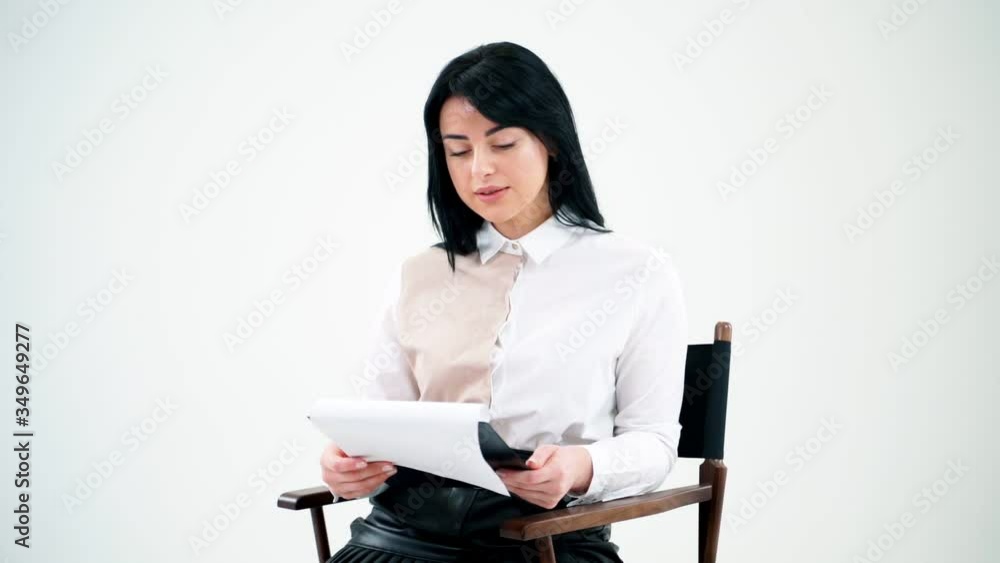 Attractive business woman reading in empty studio. Beautiful girl in white blouse and short black skirt sitting on a stool and reading paper work. Attractive business woman reading in empty studio. Beautiful girl in white blouse and short black skirt sitting on a stool and reading paper work.