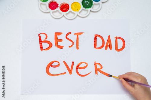 Top view of child's hand drawing handwritten text Best Dad Ever on white paper. Happy Father's Day concept.
