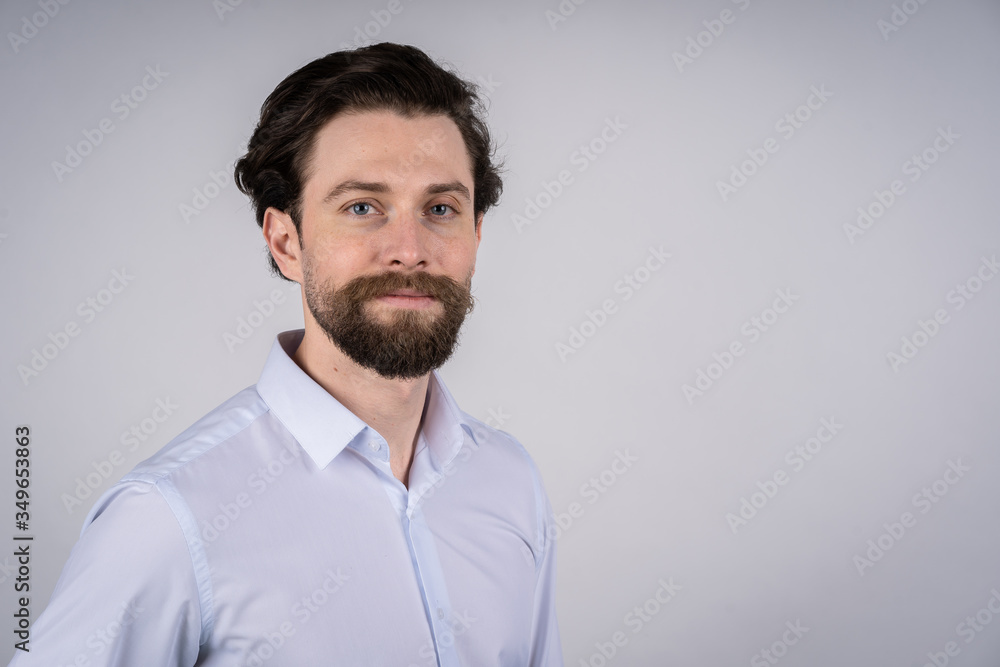 The portrait on the chest young man with a beard in a white shirt, he smiles and looks straight into the camera The portrait on the chest young man with a beard in a white shirt, he smiles and looks straight into the camera