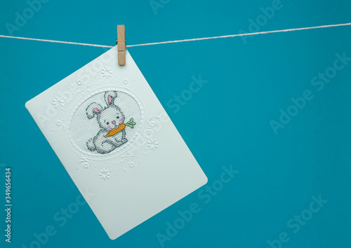 Handmade cross-stitch postcard hanging on a rope with clothespin. Bunny, rabbit.