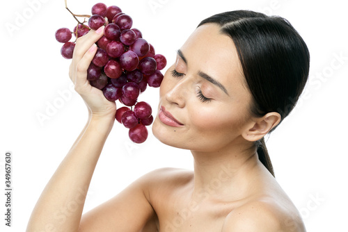 close-up portrait of a girl with clear skin and big brown eyes with soft makeup, with red grapes on a white background