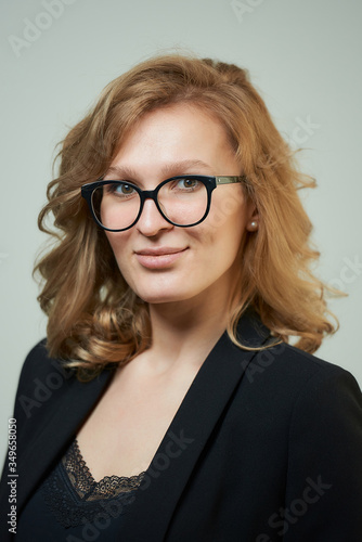 A stylish young woman in glasses dressed in a black suit with a black shirt. A close-up portrait of a happy blond lady who wears a business outfit. A concept of an office style wardrobe.