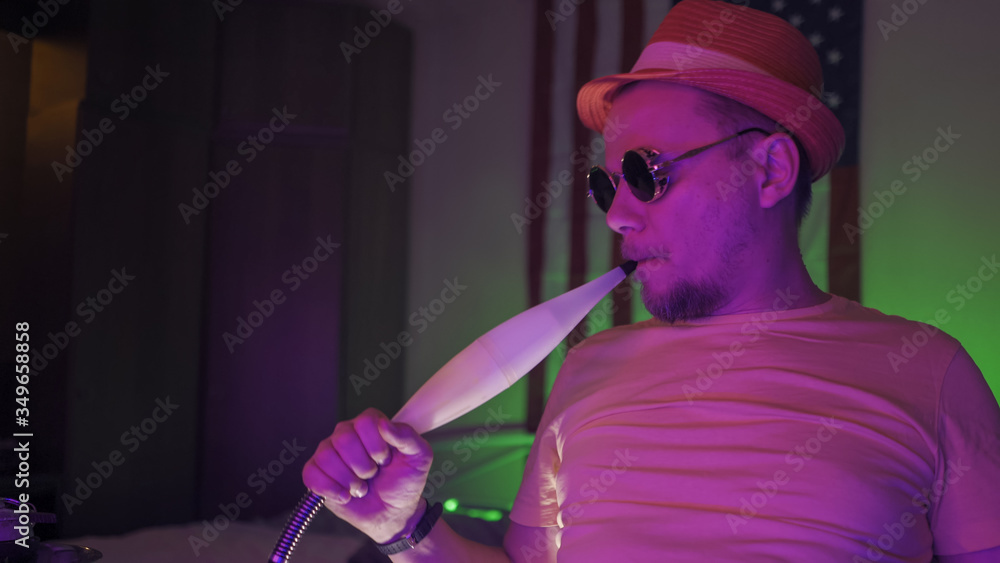 Hipster has fun self-isolation during quarantine. American man in sunglasses smokes hookah. Cheerful quarantine concept Hipster has fun self-isolation during quarantine. American man in sunglasses smokes hookah. Cheerful quarantine concept
