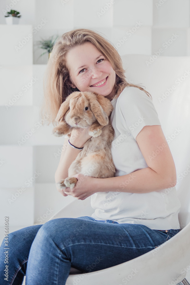 Young girl in a white jacket and jeans on a white background with a rabbit Young girl in a white jacket and jeans on a white background with a rabbit