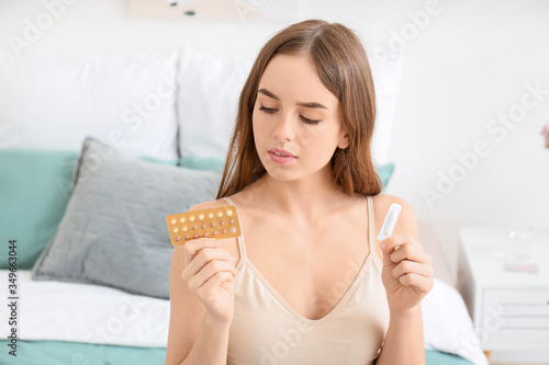 Young woman with birth control pills and contraceptive suppository in bedroom