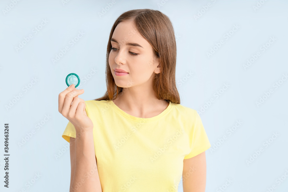 Young woman with condom on color background Young woman with condom on color background