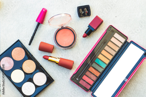 pink blush, variety lipstick and lip gloss, mascara brush, eye shadow and highlighter palette on wood table