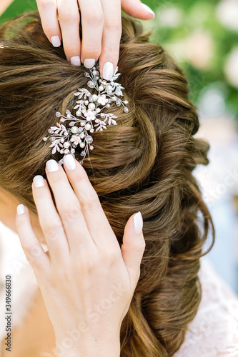 Close-up. Crop of bride's hands are correcting lewlery haircomb inserted in a complicated hairs. The view from the back. The concept of wedding jewelry, geting ready.
