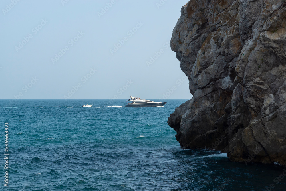 Picturesque rock off the coast of the sea. White boat on the waves