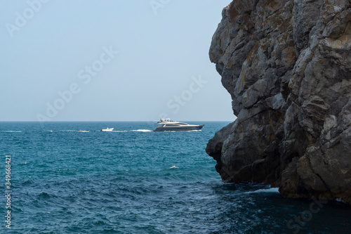 Obraz na płótnie Picturesque rock off the coast of the sea. White boat on the waves w salonie