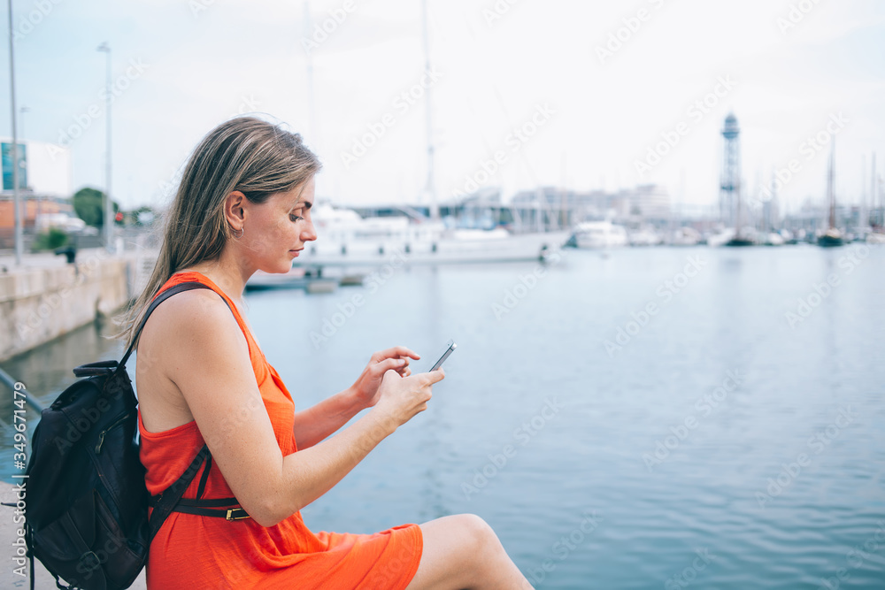 Tranquil female traveler messaging on smartphone in harbor
