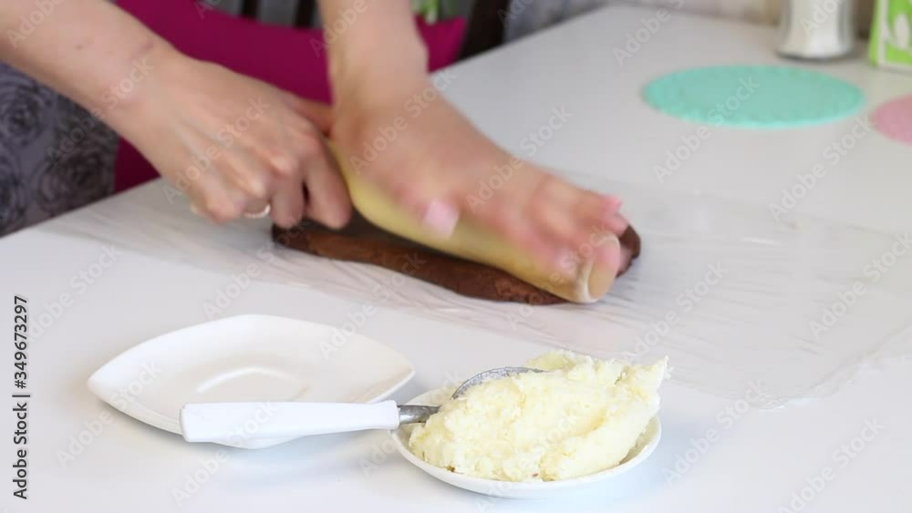 On a table the food film is developed. A woman rolls a brown lump of dough with a rolling pin. Dessert ingredients and tools. On a table the food film is developed. A woman rolls a brown lump of dough with a rolling pin. Dessert ingredients and tools.