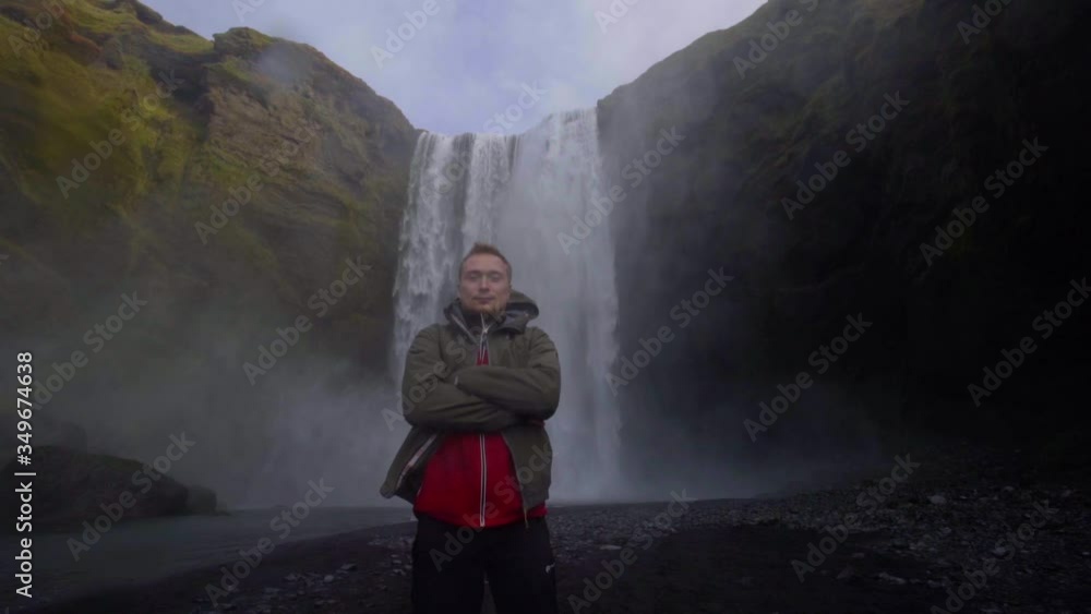 A guy poses in front of the backdrop of the huge Skogafoss waterfall A guy poses in front of the backdrop of the huge Skogafoss waterfall