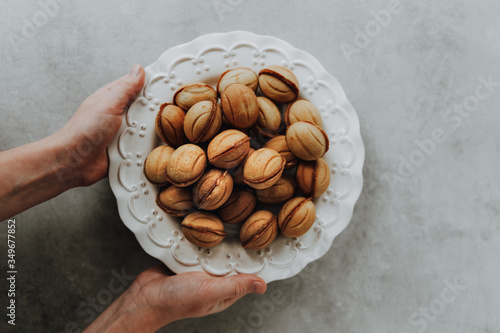 Traditional russian cookies shaped as walnut halves being filled with dulce de leche and put together. Human hands holding white plate full of cookies. photo