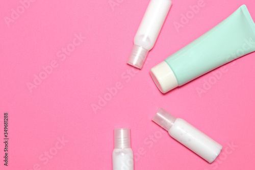 White cream tubes and one blue-green tube on light pink table. top view.
