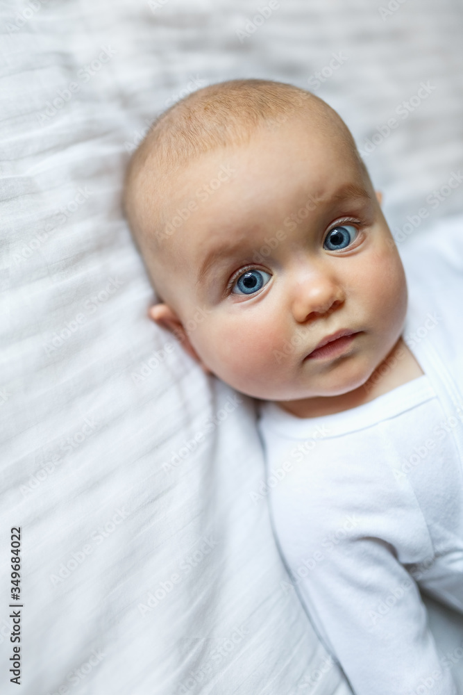 A small child of European appearance at home on a neutral light background. A beautiful pretty little girl looks at her mother in the frame. Portrait of a newborn baby close-up. A small child of European appearance at home on a neutral light background. A beautiful pretty little girl looks at her mother in the frame. Portrait of a newborn baby close-up.