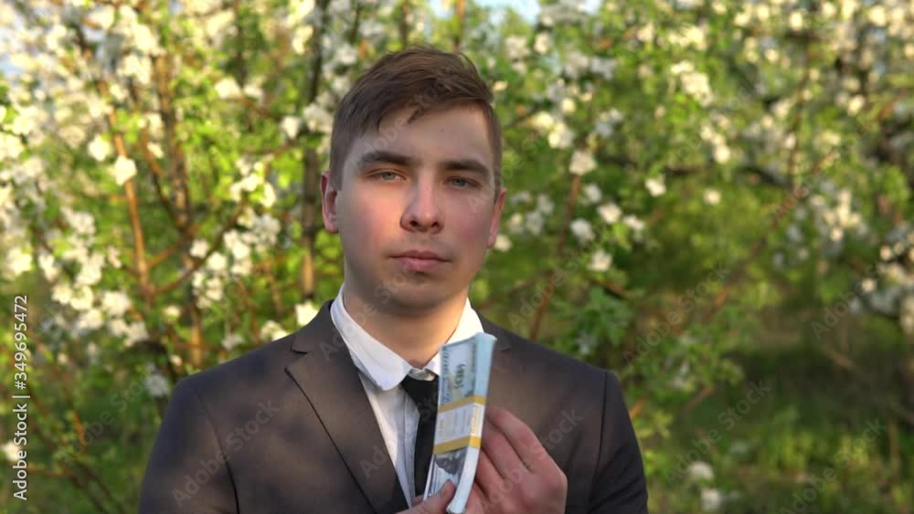 A businessman stands in the garden and sniffs dollar bills and waves them. It became hot men in a suit in nature. A businessman stands in the garden and sniffs dollar bills and waves them. It became hot men in a suit in nature.