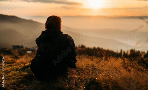 a woman sits on top of a mountain waiting for the sun to rise. Mountains in the fog, the sky is orange, yellow grass. Meditation. The balance of life. Appeasement. Peace and joy in the soul. Tourism.