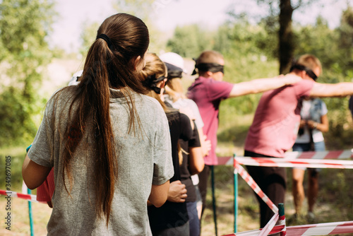 A close-up girl stands with her back and leads a team of blindfolded people. The task is to pass the maze under the leadership of the team leader. Team building exercise for a team in nature.