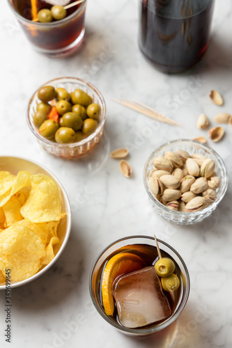 Aperitif consisting of red vermouth, olives, pistachios and chips. Marble table