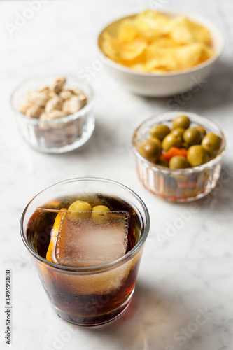 Appetizer consisting of red vermouth, olives, pistachios and chips. Marble table