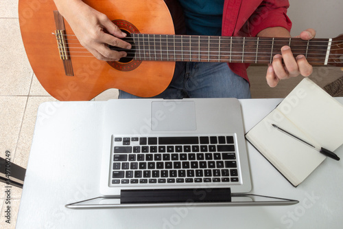 Detail of some hands playing the guitar in front of a laptop