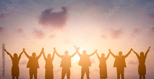 Silhouette of happy business teamwork making high hands over head in sunset sky background for business teamwork concept
