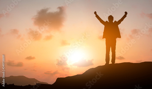 Silhouette of business man celebration success happiness stand on a mountain and sunset evening sky background