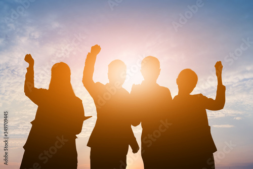Silhouette of happy business teamwork making high hands over head in sunset sky background for business teamwork concept