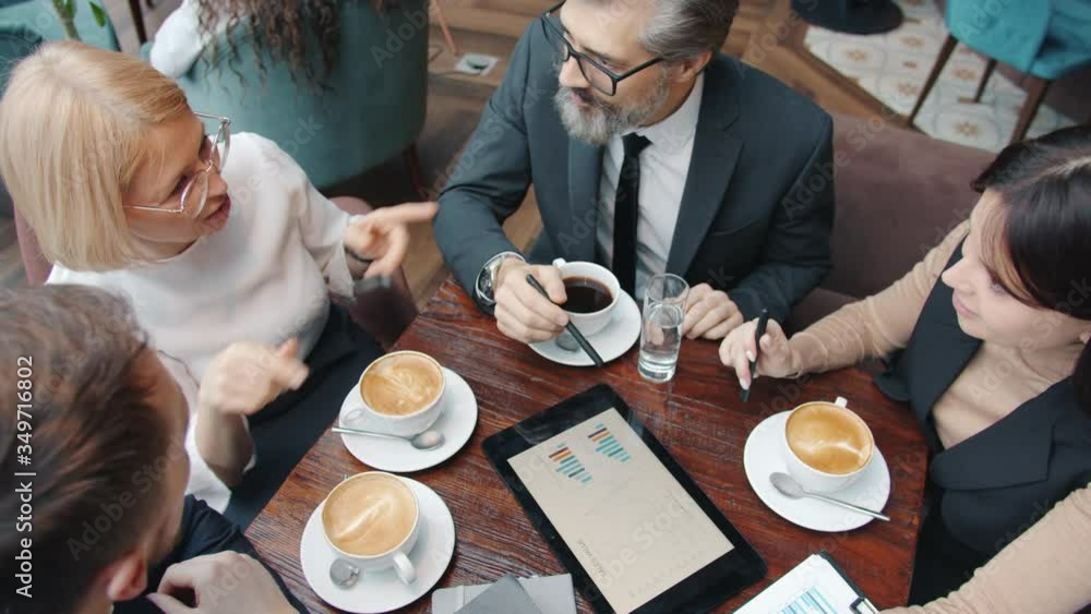 Business partners male and female are using tablet pointing at screen and talking at table in cafe. Modern technology and communication concept. Business partners male and female are using tablet pointing at screen and talking at table in cafe. Modern technology and communication concept.
