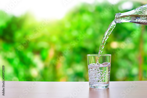 Pour water into a glass of water and bubble on natural background with copy space