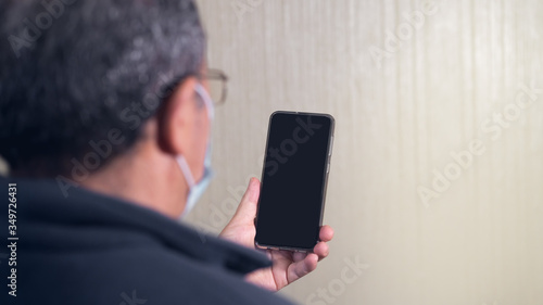 Coronavirus. Covid-19. grandpa in quarantined wearing protective mask. He is using cell phone. Pandemic, quarantine