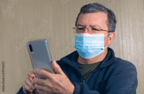 Coronavirus. Covid-19. Grandpa in quarantined wearing protective mask using cell phone. Selfie, quarantine.