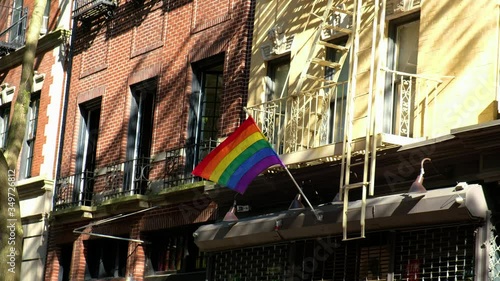LGBT plus pride flag blows in wind above storefront on a spring day city street.