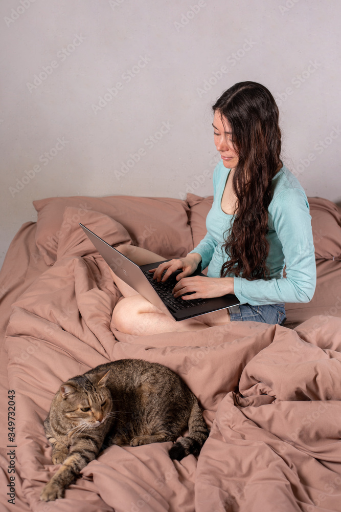 The concept of social distance and isolation. Work from home remotely over the Internet. A young woman works at home on a computer and a cat is next to her. Quarantine. The concept of social distance and isolation. Work from home remotely over the Internet. A young woman works at home on a computer and a cat is next to her. Quarantine.
