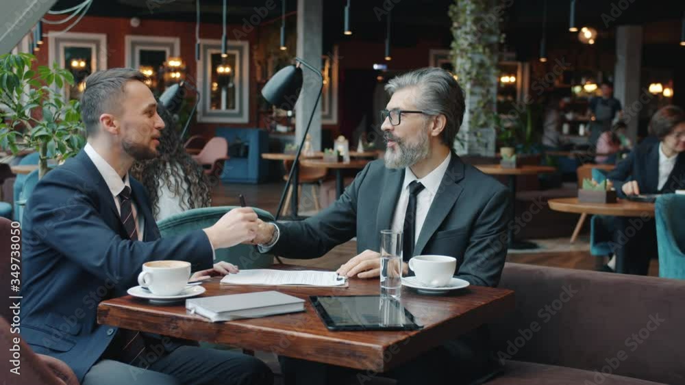 Businessmen in formalwear are using smartphones touching screen sitting at table in cafe concentrated on modern devices. Communication and gadgets concept. Businessmen in formalwear are using smartphones touching screen sitting at table in cafe concentrated on modern devices. Communication and gadgets concept.