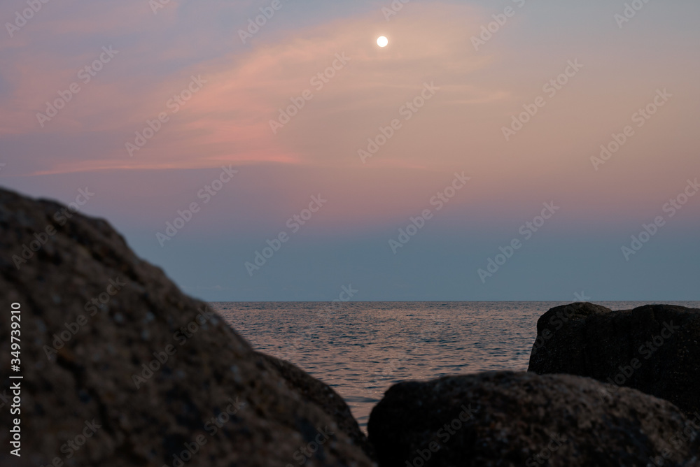 Full moon at spectacular sunset over rocks and sea