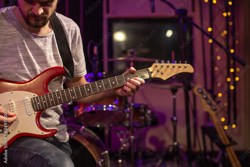 Fototapeta premium A man plays an electric guitar in a recording Studio. A rehearsal room for musicians with a drum kit in the background.