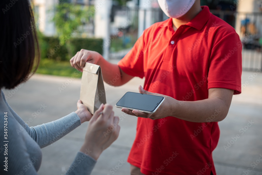 Deliver man wearing face mask in red uniform handling bag and  parcel box give to female costumer Postman and express grocery delivery service during covid19.